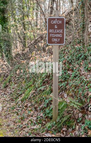 A catch and release signage for fishing only posted on the trail along the lake with the woodlands in the background at the park Stock Photo