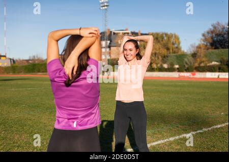 two young women doing stretching on the grass of a running track before playing sports Stock Photo