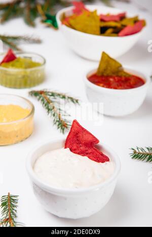 Christmas festive snacks. Green and Red Tortilla crisps in shape of Christmas tree in bowls with sour cream, salsa, guacamole, cheese dipping sauces Stock Photo