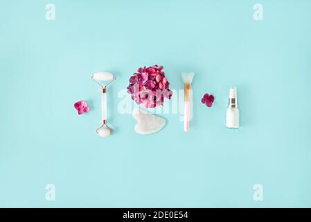 Top view composition with pink jade roller face massager, gouache scraper, brush, natural serum and hydrangea flower on the light blue turquoise Stock Photo