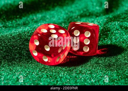 Red acrylic transparent dices for games. Two gambling translucent dices on green velvet surface, close up. Stock Photo