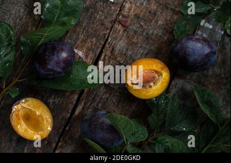 Two pieces of plum on old wooden table near green leaves. Stock Photo