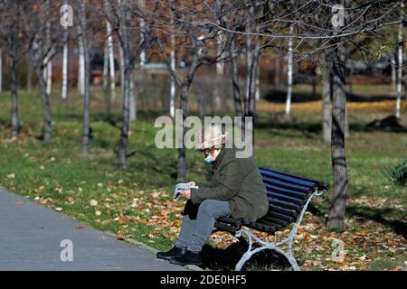 Bucharest, Romania. 27th Nov, 2020. A woman wearing a face mask sits on the bench at a park in downtown Bucharest, Romania, Nov. 27, 2020. The Romanian authorities have imposed a one-month curfew throughout the country from Nov. 9. Residents are not allowed to leave their homes from 11 p.m. to 5 a.m. without special circumstances. Credit: Cristian Cristel/Xinhua/Alamy Live News Stock Photo