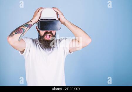 Guy in helmet works as engineer in virtual reality. 3D design concept. Man with beard in VR glasses shocked and disappointed, light blue background. Architect or engineer with virtual reality glasses. Stock Photo