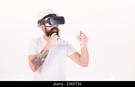 Bearded man in safety helmet isolated on white background. Brutal architect with stylish beard finishing project using 3D visualisation. Bearded builder with VR headset, digital innovations concept. Stock Photo