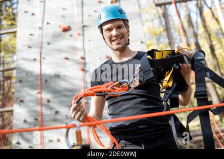 Handsome man wearing safety equipment for climbing at amusement park, preparing for climbing on the wall Stock Photo