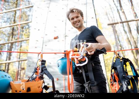 Handsome man wearing safety equipment for climbing at amusement park, preparing for climbing on the wall Stock Photo