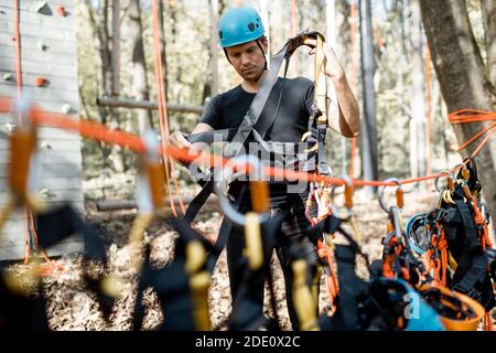 Handsome man wearing safety equipment for climbing at amusement park, preparing for climbing on the wall Stock Photo