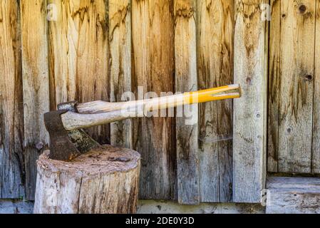 Two wooden axes stuck in the wood chopping trunk. In the background, a wooden wall of the old house. Stock Photo