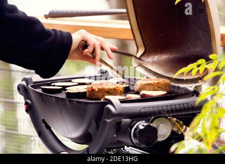 Eggplants and veggie burgers are grilled on portable barbeque and about to be turned with tongs Stock Photo