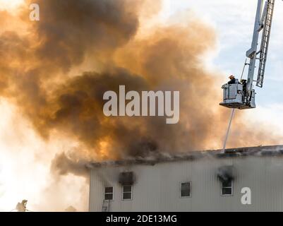 Two firemen fighting building fire from bucket above. A hose sprays water through the smoke. The firemen are wearing breathing apparatus. Stock Photo