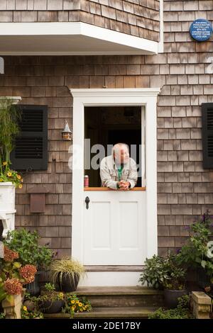 A man peers down the street from a half door in Provincetown, Massachusetts. Stock Photo