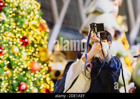Selected focus of couple in protective mask selfie in front of a Christmas tree. Stock Photo