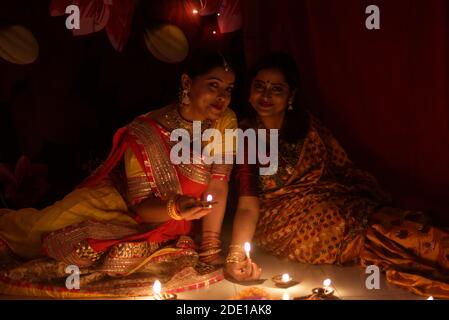 Two beautiful Indian Bengali women in Indian traditional dress lightening Diwali lamps sitting on the floor on Diwali evening. Indian lifestyle Stock Photo