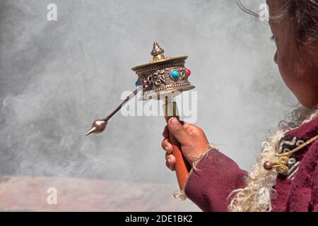 Little Tibetan girl praying with prayer wheel and smoke from incense in Drepung Monastery, one of the great three Gelug university monasteries of Tibe Stock Photo
