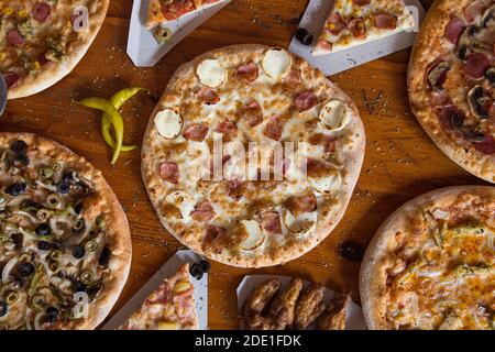 Pizza dinner. Flat of various kinds of Italian pizza on rustic wooden table, top view. Quick lunch, celebration, meeting concept. Stock Photo