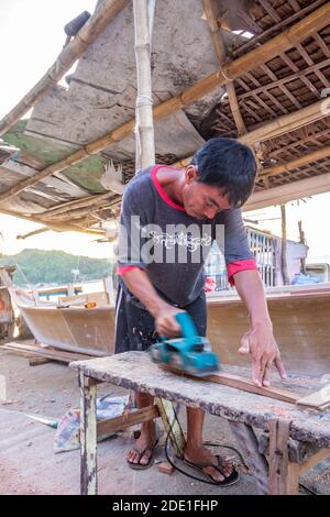 A Filipino wood worker working on a piece of wood for his boat being constructed in Batangas, Philippines Stock Photo