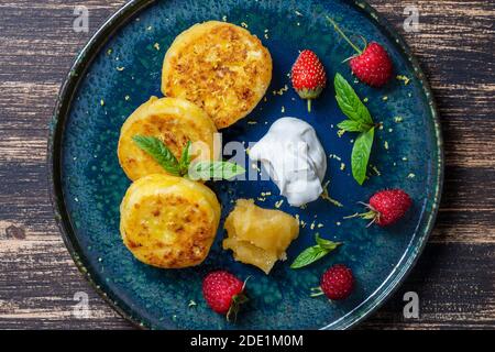 Cheesecakes with mint, raspberries, honey and sour cream. Delicious dessert, ukrainian food. Close up, top view Stock Photo