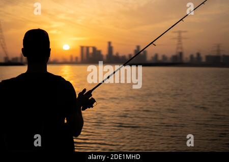 Fisherman casting lure towards the sunset and watching the skyline of Abu Dhabi Stock Photo