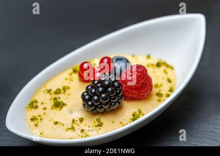 Dessert of whipped cream, raspberries, blueberries, blackberries and red currants in a porcelain tray close-up. Stock Photo