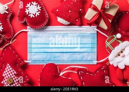 Christmas decorations and a disposable medical mask on a red background, top view. A concept on quarantine during the holidays due to the pandemic. Stock Photo