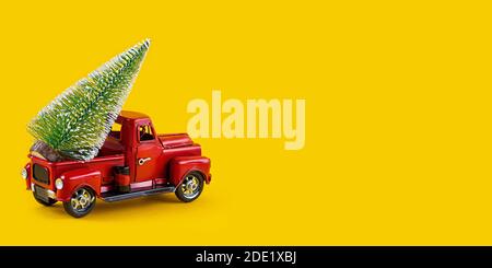 Red retro toy truck with Christmas tree on truck body on yellow background. Delivery, christmas, New Year concept. Vintage toy model car with Christma Stock Photo