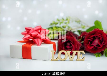 gift box with a red bow on a background of flowers roses and bokeh with the text wooden letters love for the holiday valentine's da Stock Photo