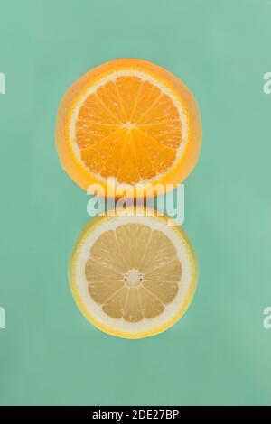 The pulp of a cut orange next to the reflection in a cut lemon. Citrus fruits on pastel-colored background with paper texture. Stock Photo