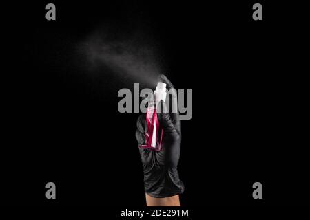 A female hand in a rubber black glove sprays a hand antiseptic from bottle on a black background. Banner. Coronovirus, Covid-19, Quarantine, Pandemic