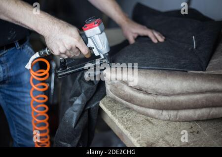 Furniture making process. Young man sheathes part of the sofa with a stapler on the desktop Stock Photo