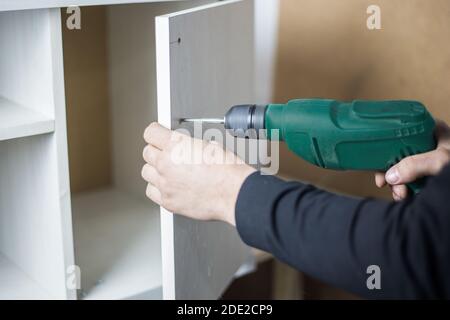 The master holds a puncher in his hands and drills a hole. Power tool rental concept. Furniture manufacturing Stock Photo