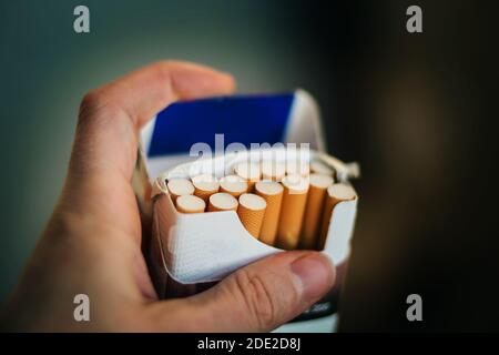 A man holds an open pack full of cigarettes with orange filters in his hand. The harm from Smoking. Stock Photo