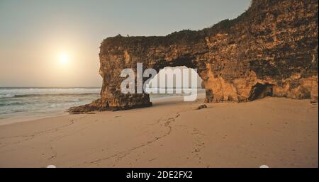 Aerial view of sun over rock wall with hole at sand beach sea shore. Unique geological formation at Bawana Beach, Sumba Island, Indonesia, Asia. Nobody nature landscape with ocean water waves Stock Photo