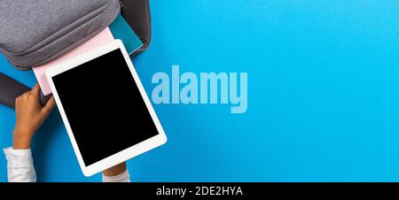 Kid hands taking digital tablet computer from gray backpack over light blue background. Top view Stock Photo