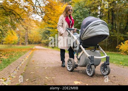 Mom with stroller walks in the fresh air of the autumn park Stock Photo