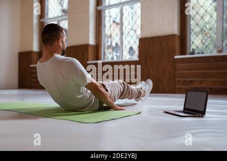 Self isolated and motivated young man warm-up doing special exercises for muscles. Self motivated young handsome bearded man looking for online work Stock Photo