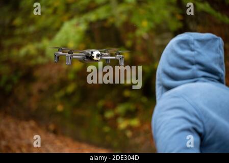 Selective focus shot of a mysterious man in a hoodie examining a flying drone in front of him Stock Photo