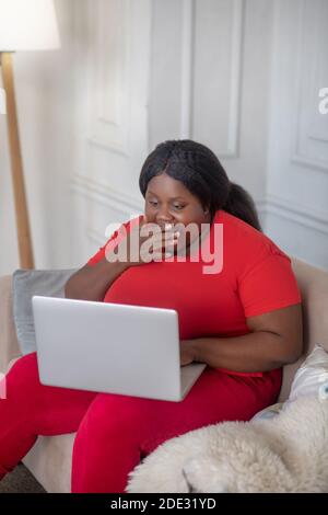 African american woman sitting in her room with a laptop and looking surprised Stock Photo