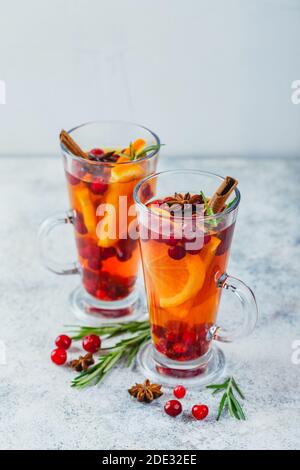 Hot tea with orange slices, cranberries and rosemary in tall glasses. Hot drinks for winter and Christmas Stock Photo