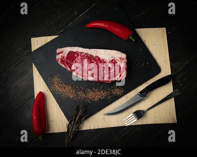 Raw ribeye beef steak cooking with ingredients on a black plate. Top view.  Stock Photo
