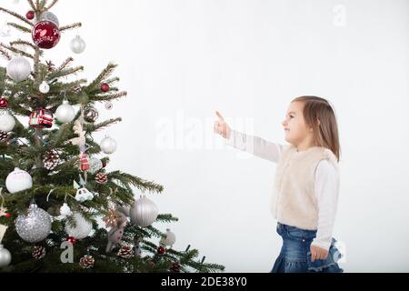 Cheeky toddler girl pointing towards the tip of the Christmas tree Stock Photo