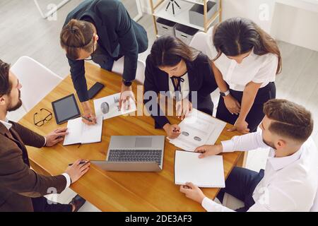 Sales team gather around office desk, analyze financial data and do paperwork using laptop computer Stock Photo