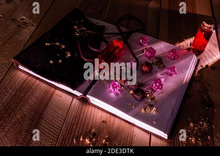 Pink and red role playing dice on top of a leather bound notepad. Two glass bottles with red liquid on a wooden table Stock Photo