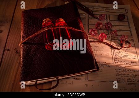 Image of a leather bound tome with on top two bottles with red liquid. Role playing dice, pencils and a note sheet for table top gaming Stock Photo