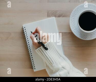 woman writing in notebook on wooden table, hand in sweater holding pen, Stock Photo