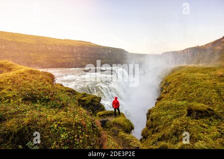 Back view of explorer enjoying view of amazing waterfall in highlands at sunset Stock Photo