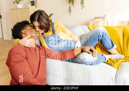 Husband kissing his pregnant wife on a sofa. Interracial couple concept Stock Photo