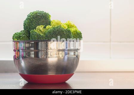 Stainless steel bowl filled with broccoli sprigs on table in a kitchen Stock Photo