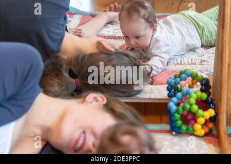 A mother interacting and playing with her 4 month old baby daughter, with both lying down on a play mat with a mirror behind, UK Stock Photo