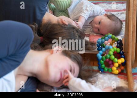 A mother interacting and playing with her 4 month old baby daughter, with both lying down on a play mat with a mirror behind, UK Stock Photo